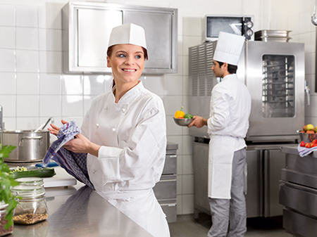 Eine junge Frau und ein junger Mann in Arbeitskleidung stehen in einer Großküche.